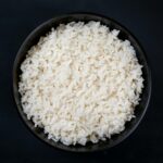 A bowl filled with freshly cooked white rice, shot from above against a dark background for contrast.