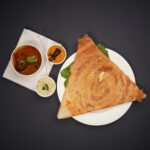 Top view of masala dosa with chutneys and sambar on a black background. Perfect for food photography.