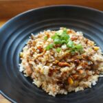 Delicious homemade fried rice with scallions and sauce on a black plate.