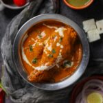 Mouth-watering butter chicken curry garnished with cream and herbs, served in a stainless steel bowl.